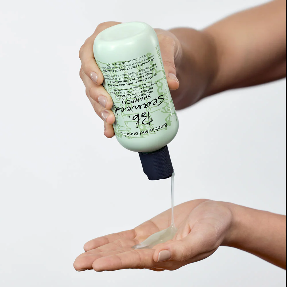 Hand holding a bottle of Suave shampoo over an open palm with a white background. Bumble and Bumble Seaweed Nourishing Shampoo 8.5oz bottle, gentle shampoo that hydrates, nourishes, and cleanses hair while enhancing softness, shine, and manageability.