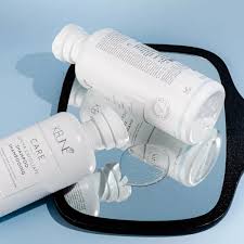 Two bottles of skincare product on a black tray with a blue background. Keune Care Derma Exfoliate Shampoo 10oz bottle, gentle exfoliating shampoo that removes buildup, soothes the scalp, and leaves hair clean, refreshed, and healthy.