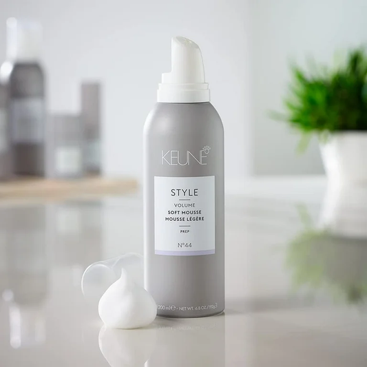 Keune hair product bottle on a blurred background. Keune Style Volume Soft Mousse 6.9oz can, lightweight styling mousse that adds volume, body, and natural movement to all hair types without stiffness