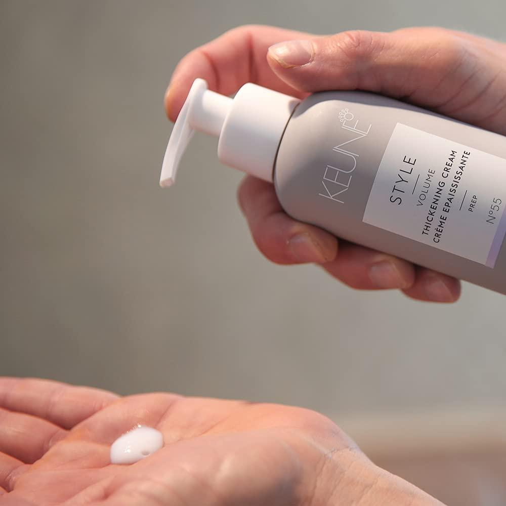 Hand holding a bottle of Keune Style Volume Thickening Cream with cream on palm