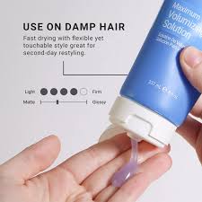 Hand holding a bottle of hair product with text on use and features. Loma Maximum Volumizing Solution 8oz bottle, lightweight styling solution that adds lift, body, and fullness to hair while enhancing texture and manageability.
