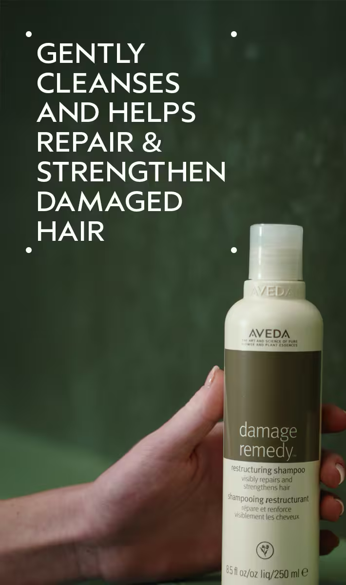 Aveda damage remedy shampoo bottle held by a hand with text about hair care on a green background. Aveda Damage Remedy Restructuring Shampoo 8.5oz bottle, gentle shampoo that repairs, strengthens, and nourishes damaged hair while restoring softness and shine.