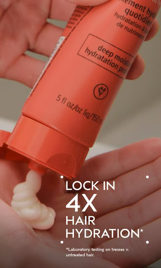 Hand holding a red hair care product with visible cream, labeled 'Lock in 4X Hair Hydration'. Aveda Nutriplenish Deep Moisture Conditioner 8.5oz bottle, rich conditioner that deeply hydrates, nourishes, and restores softness and shine to dry or damaged hair.