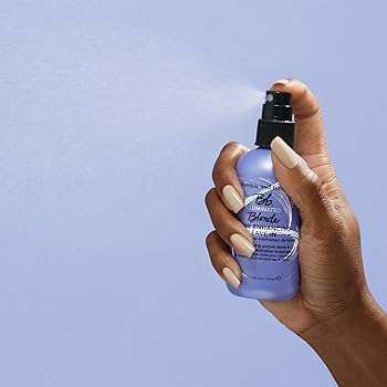 Hand holding a purple bottle of Bumble and Bumble Illuminated Blonde Tone Enhancing Leave-In 4.2oz bottle, lightweight leave-in treatment that enhances blonde tones, adds shine, and improves hair manageability.