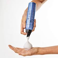 Person holding a blue and black bottle with a white pump, applying a white cream to their hand. Bumble and Bumble Thickening Full Form Soft Mousse 5oz can, lightweight mousse that adds volume, body, and fullness while keeping hair soft, flexible, and touchable.