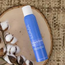 Blue bottle labeled 'LOMA' on a wooden surface with cotton fibers. Loma Texture & Finishing Spray 5.4oz bottle, lightweight spray that adds texture, volume, and hold while finishing styles with natural movement and shine.
