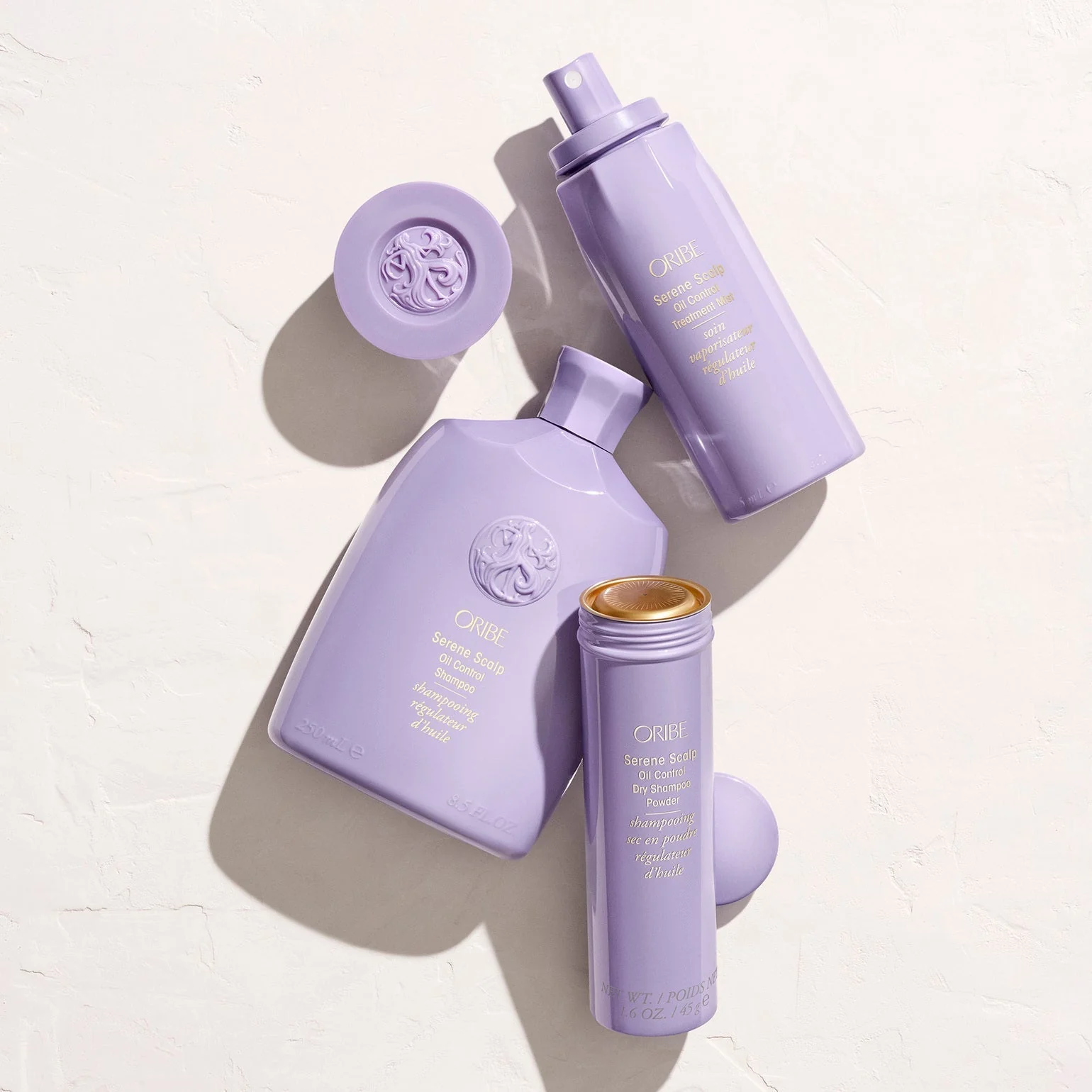 Set of purple skincare bottles with a brand logo on a light background. Oribe Serene Scalp Oil Control Treatment Mist, lightweight spray that balances oil, soothes the scalp, and refreshes hair for a clean, healthy look.