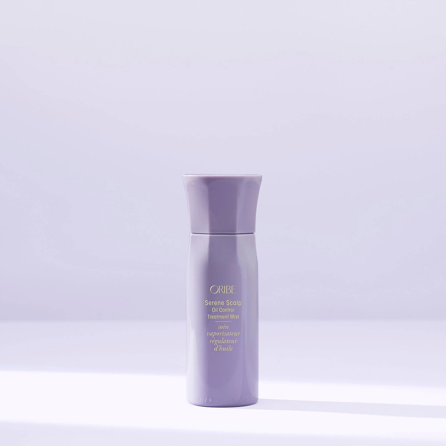Purple haircare bottle with text on a light purple background. Oribe Serene Scalp Oil Control Treatment Mist, lightweight spray that balances oil, soothes the scalp, and refreshes hair for a clean, healthy look.